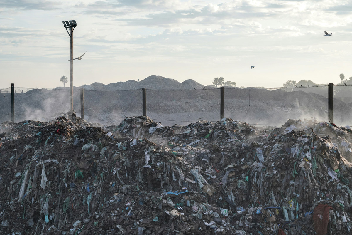 A pile of garbage on a dump site with birds flying over
